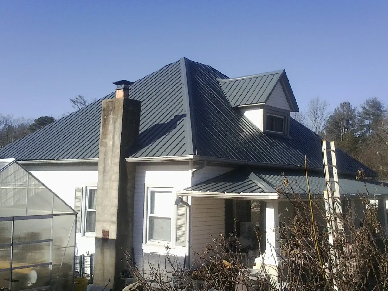 Dark blue standing seam metal roof on a white farmhouse with dormer — Slate & Tile Roof Repair by Roofing Brothers in Philo