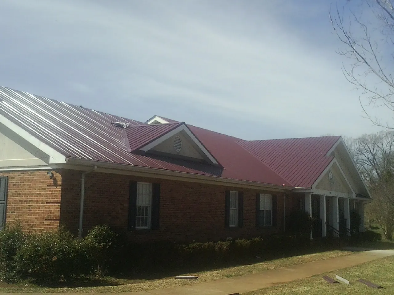 Red metal roof with gabled entries on a long brick building, from a Hail Damage Roof Repair job in Philo