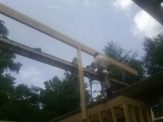Carpenter setting a ridge beam over a new addition frame in Philo