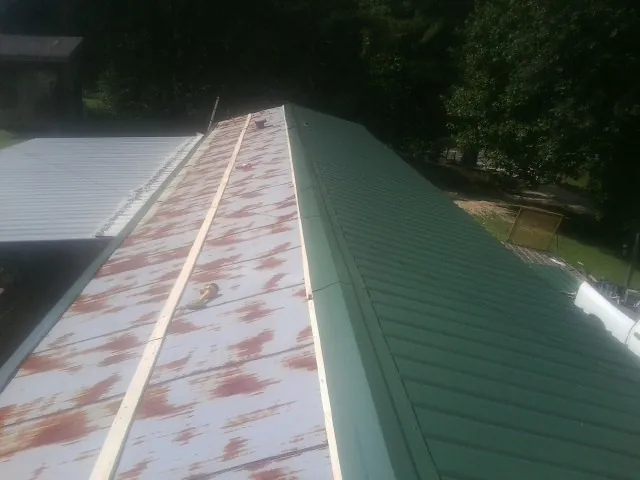Old rusted panels beside newly installed green metal roofing — Wind Damage Roof Repair by Roofing Brothers in Philo