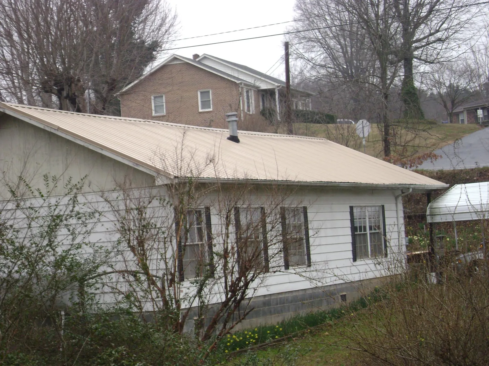 Tan metal roof on a white sided house set into a hillside — Commercial Roofing by Roofing Brothers in Philo